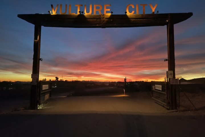 Vulture City entrance silhouetted against a vibrant sunset sky.