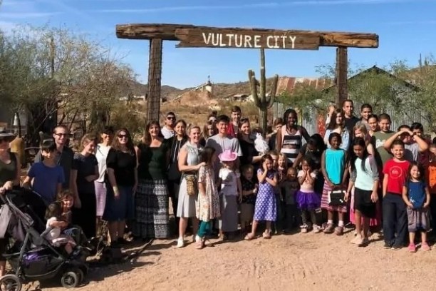 Group photo of people under 'Vulture City' sign in a rustic outdoor setting.