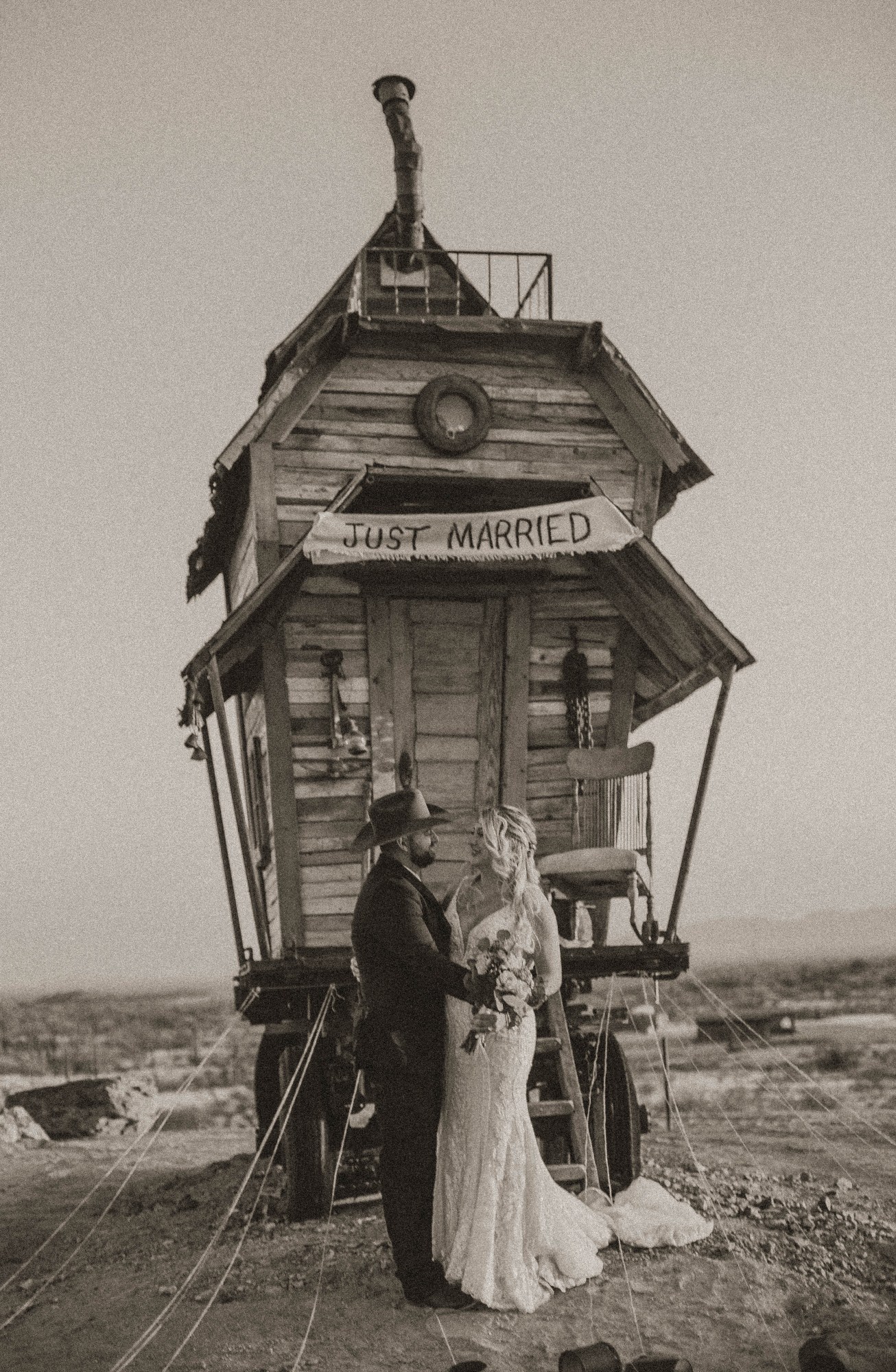 Sepia photo of a couple in wedding attire by a rustic carriage with 'Just Married' sign.